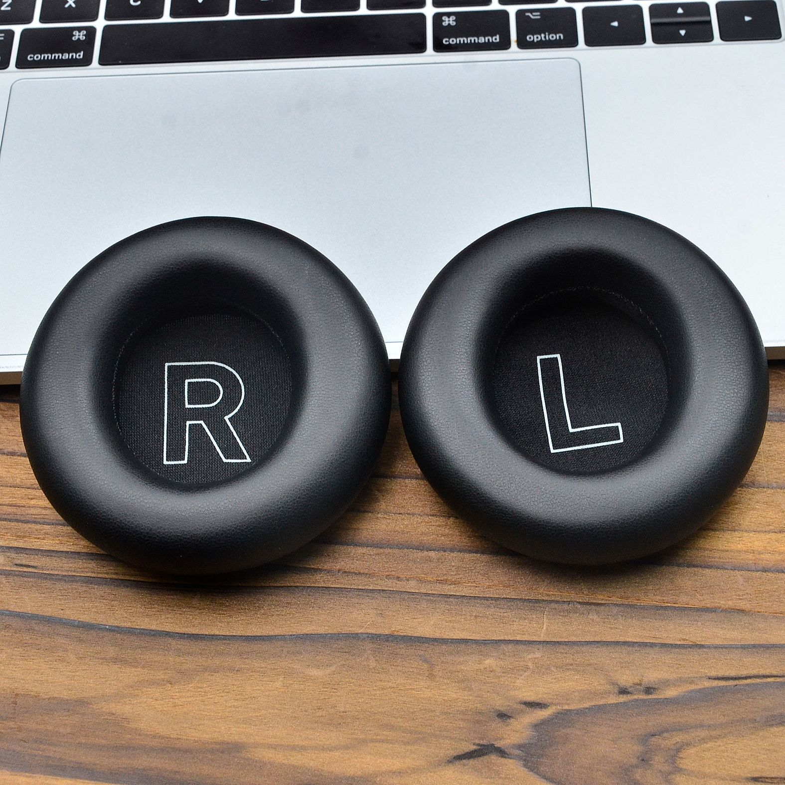 Dwie czarne nauszniki słuchawkowe z białymi oznaczeniami 'R' i 'L', na laptopie.