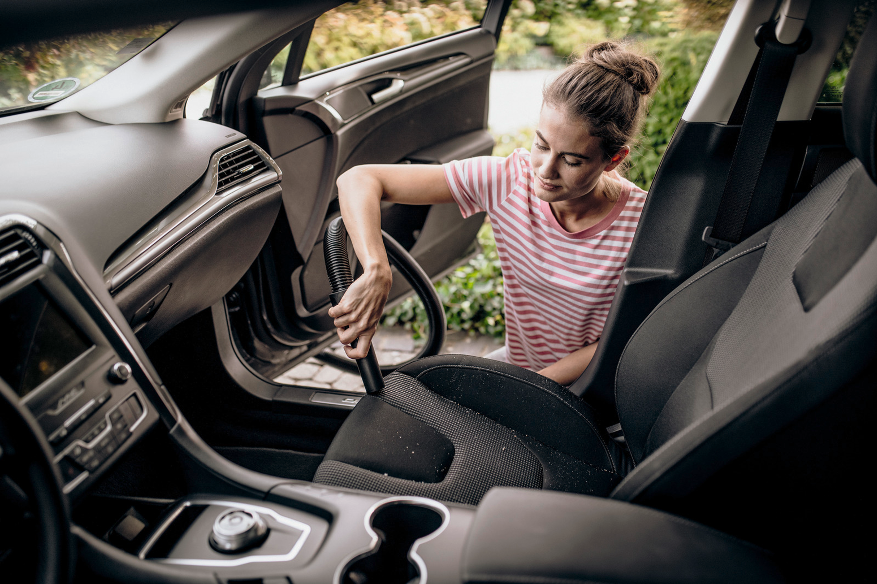 Donna che aspira l'interno di un'auto, usando un aspirapolvere portatile.