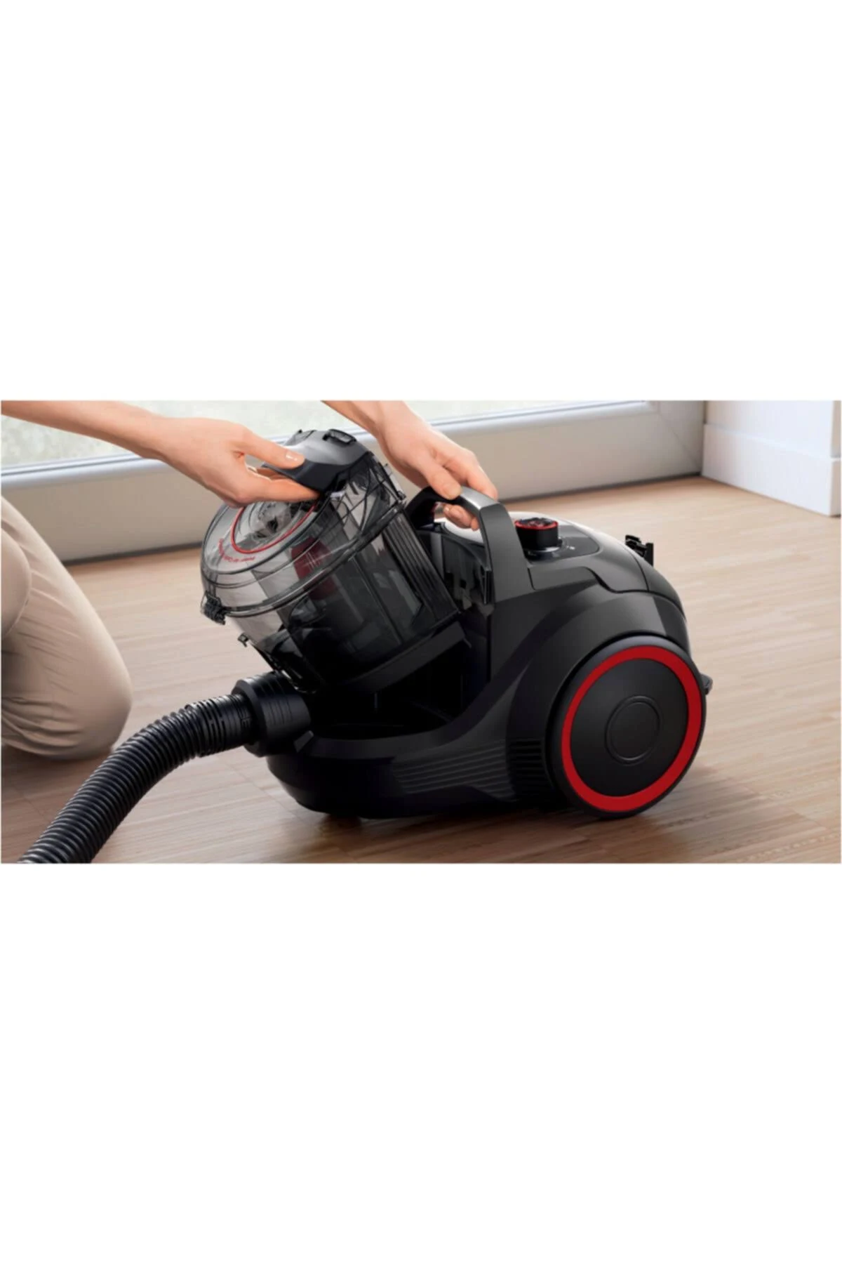 Una persona vaciando una aspiradora. La aspiradora es negra con detalles rojos y está sobre un piso de madera.