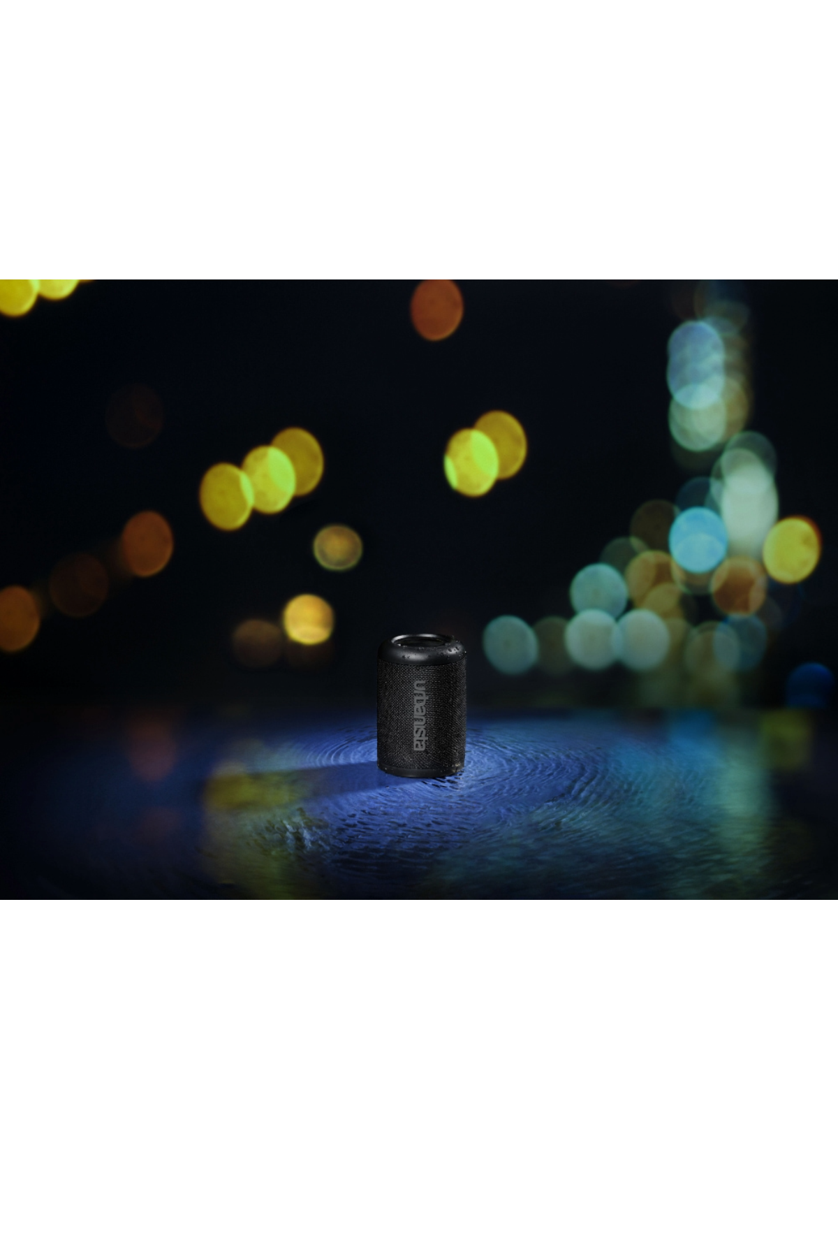 Czarny głośnik walcowy. Tekst: urbansista. W ciemnym otoczeniu. Rozmyte światła w tle.