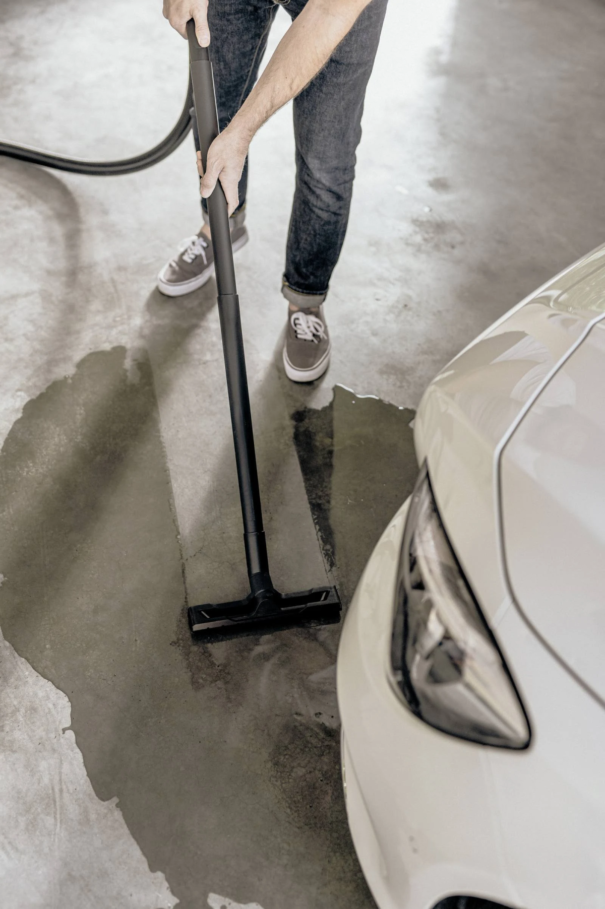 Persona aspirando un suelo de garaje mojado con un coche aparcado.