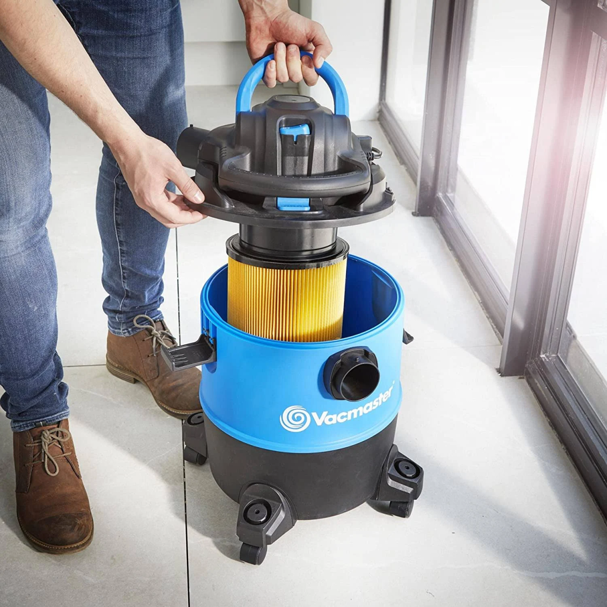 Persona che rimuove il filtro da un aspirapolvere Vacmaster blu e nero.