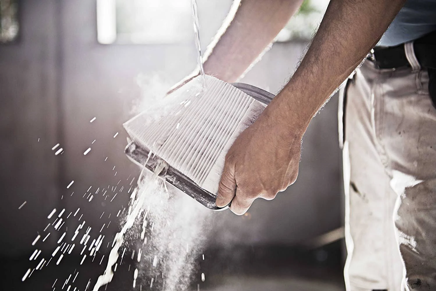 Una persona lava un filtro con acqua. Il filtro è bianco e rettangolare.