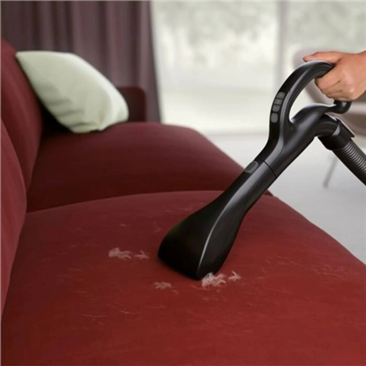 Odkurzacz czyszczący czerwoną sofę. Sofa ma na sobie białe włosy.