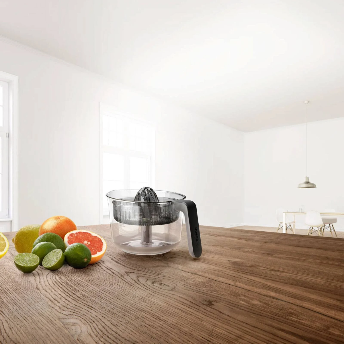 Una mesa con fruta y un exprimidor. En el fondo, una habitación brillante y vacía.