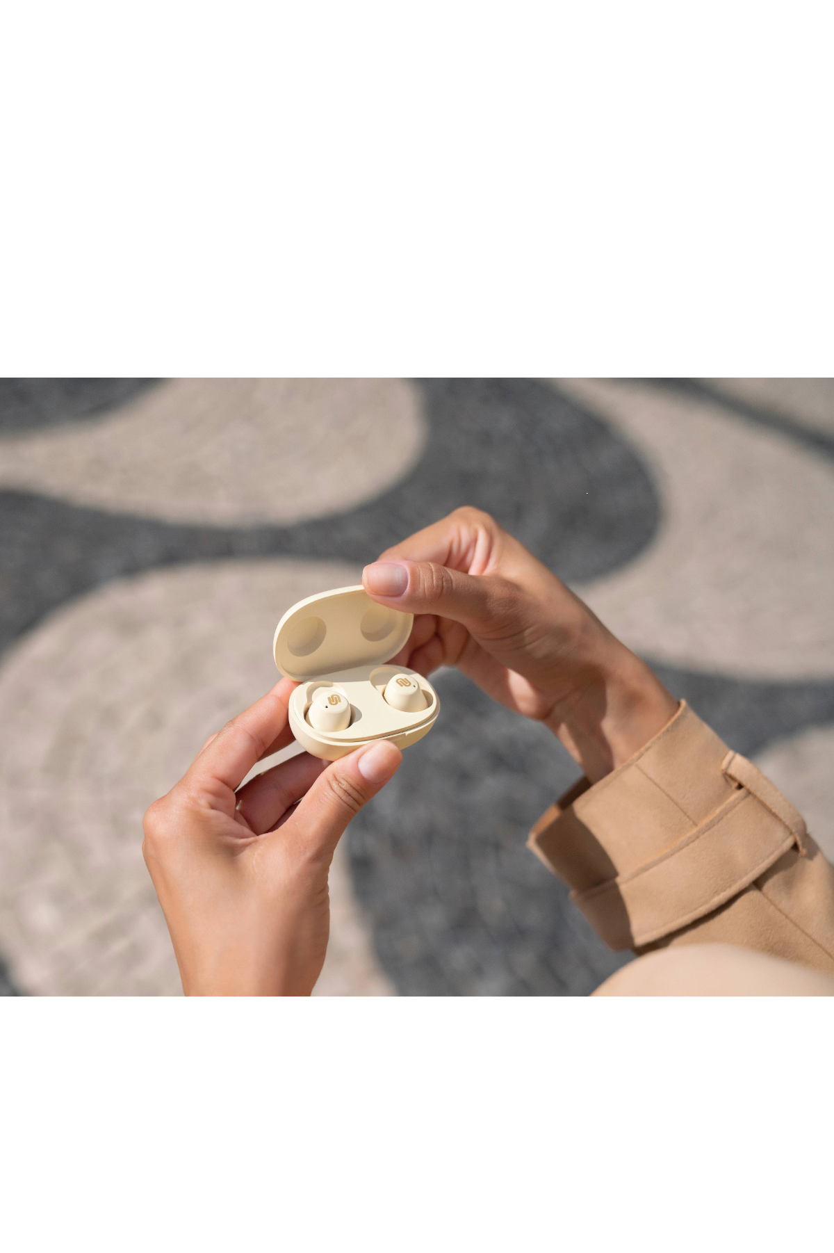 Osoba trzymająca beżowe etui z dwoma beżowymi słuchawkami, gotowe do użycia.