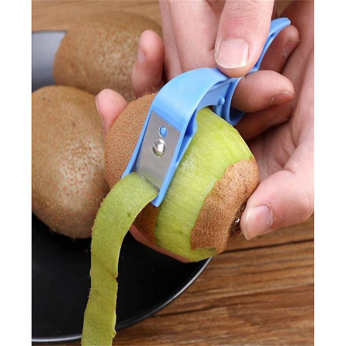 Eine Person schält eine Kiwi mit einem blauen Schäler. Zwei weitere Kiwis liegen neben der geschälten.