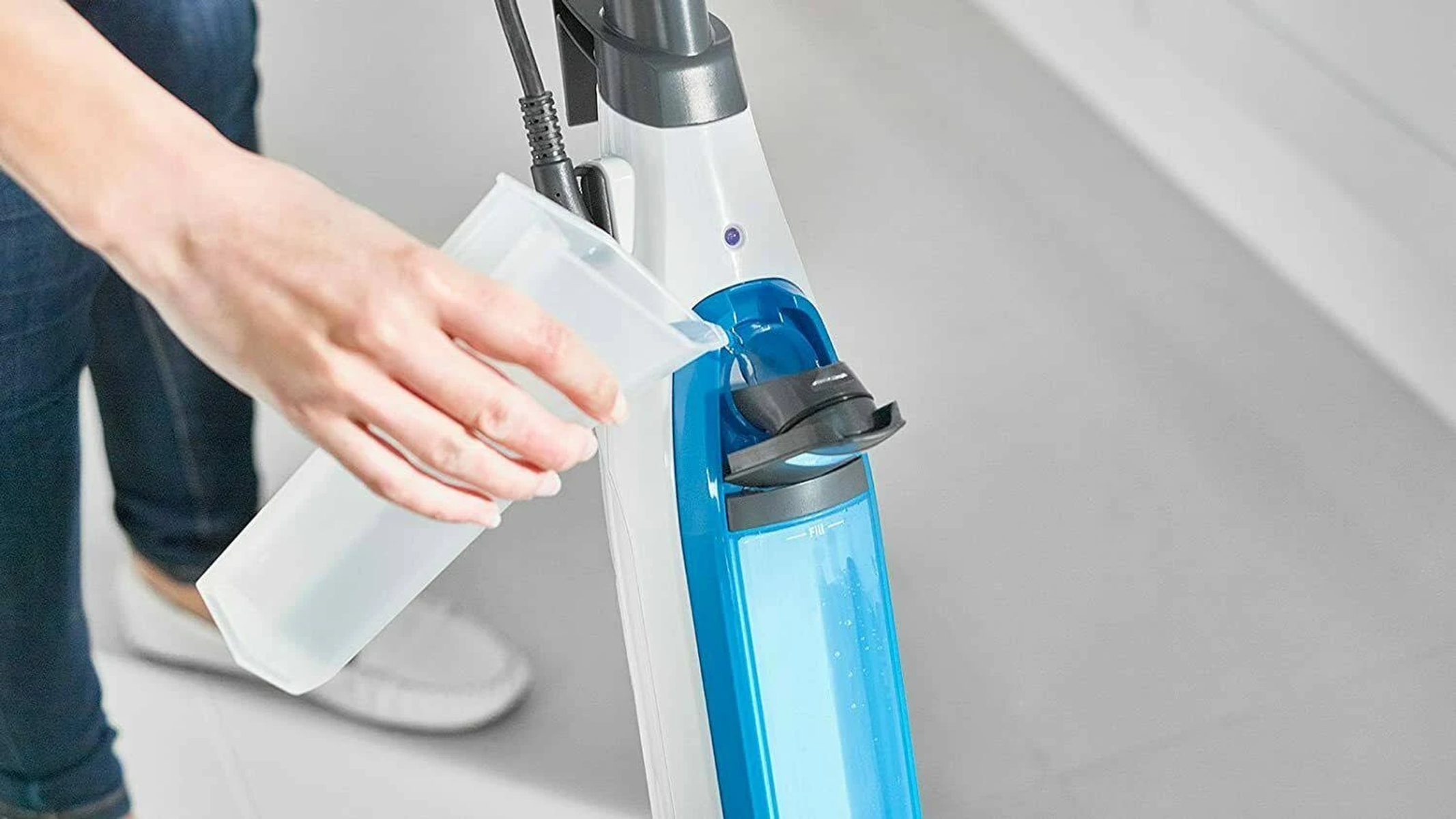Osoba wlewa wodę do zbiornika na wodę mopa parowego.