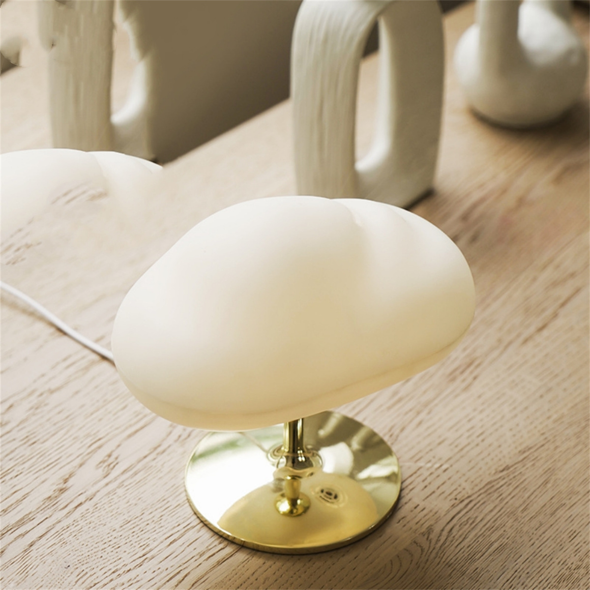 Eine cremefarbene Lampe mit einzigartiger, wolkenartiger Form, auf goldfarbener Basis, auf Holz.