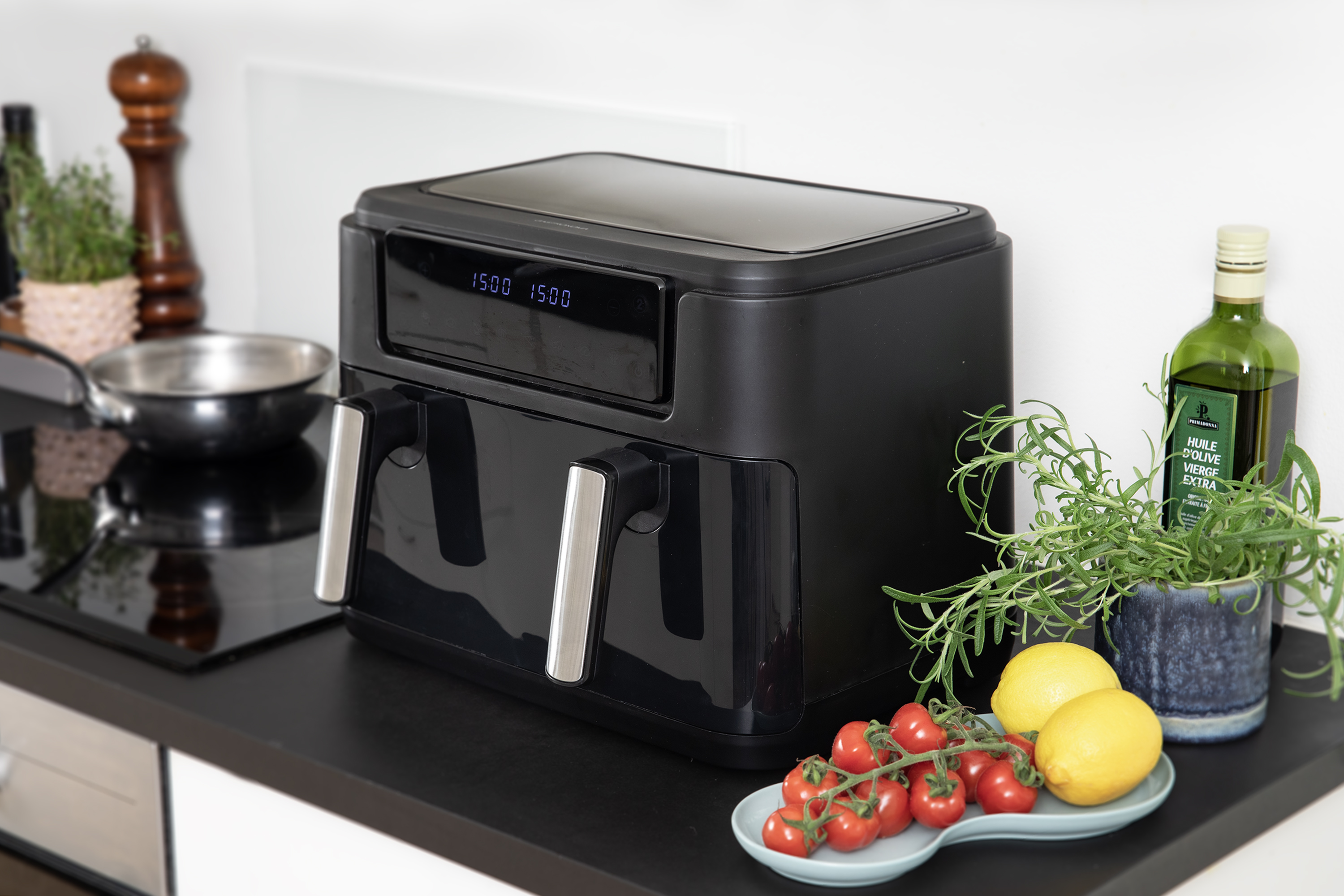 Czarna frytkownica powietrzna z cyfrowym wyświetlaczem na blacie, z rozmarynem, pomidorami i cytrynami.