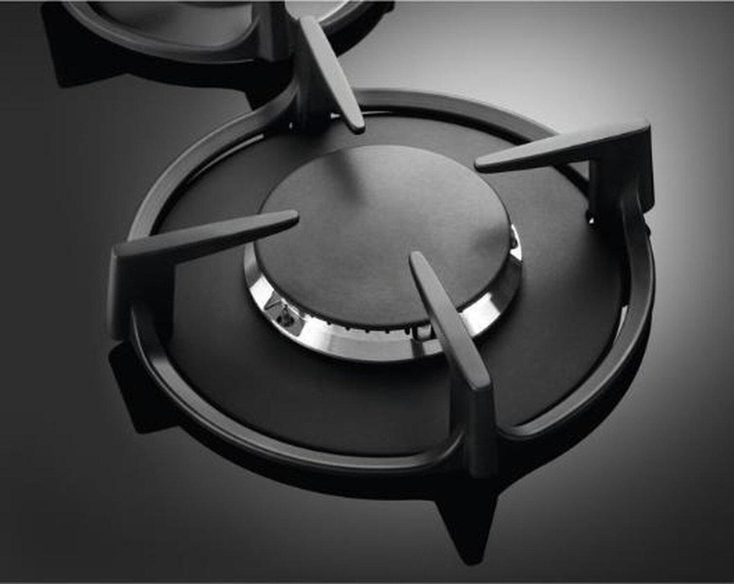 Zbliżenie czarnego palnika kuchenki gazowej z czterema zębami. Metaliczne srebro pośrodku.