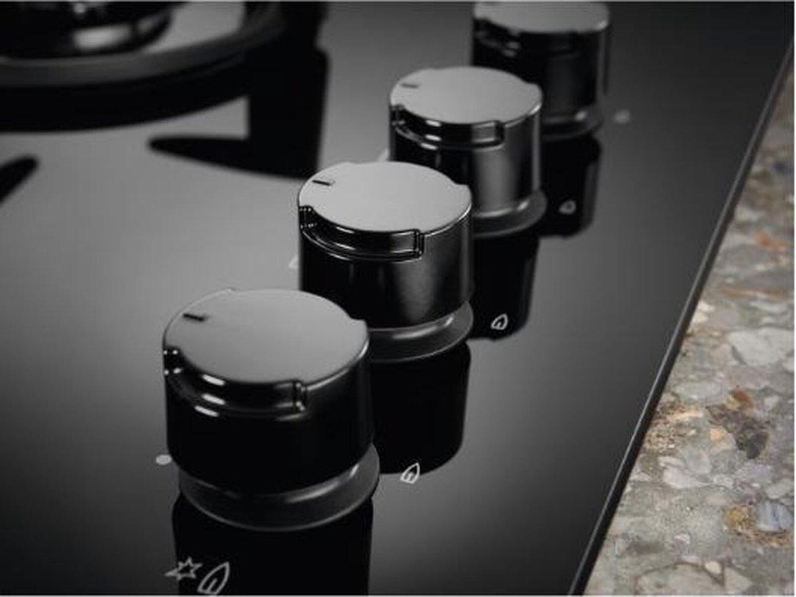 Pokrętła sterowania płyty grzewczej. Czarne pokrętła na czarnej szklanej powierzchni. Cztery pokrętła w rzędzie.