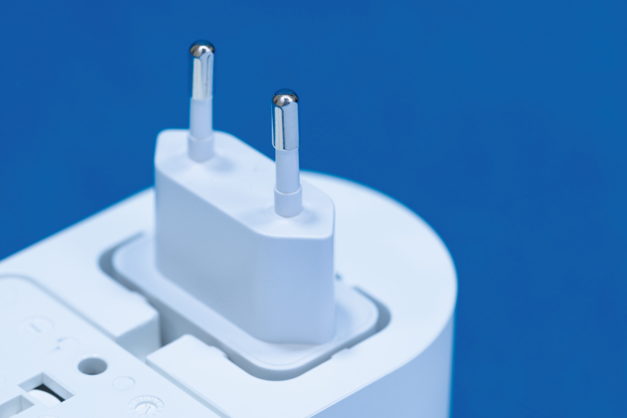 Nahaufnahme eines weißen Netzadapters mit zwei Stiften auf blauem Hintergrund.