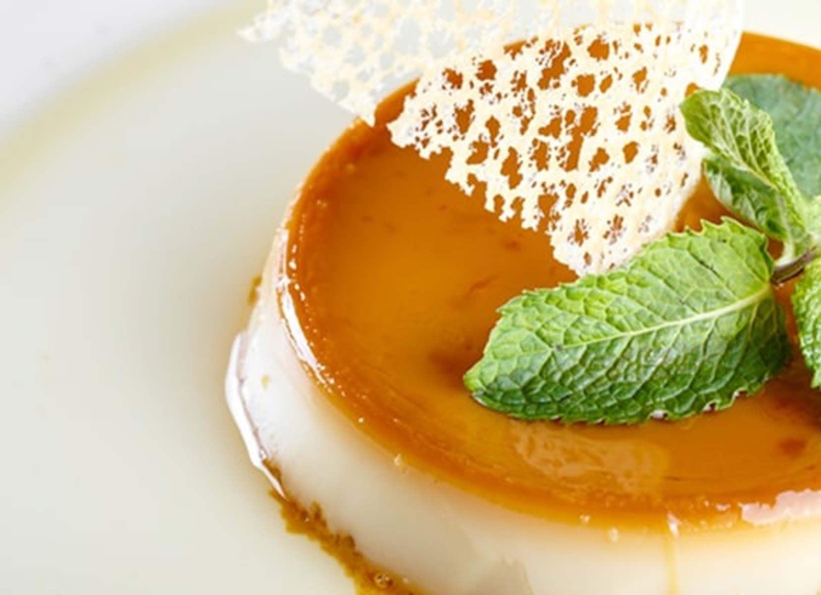 Flan dessert con glassa al caramello e foglie di menta, con un biscotto decorativo.