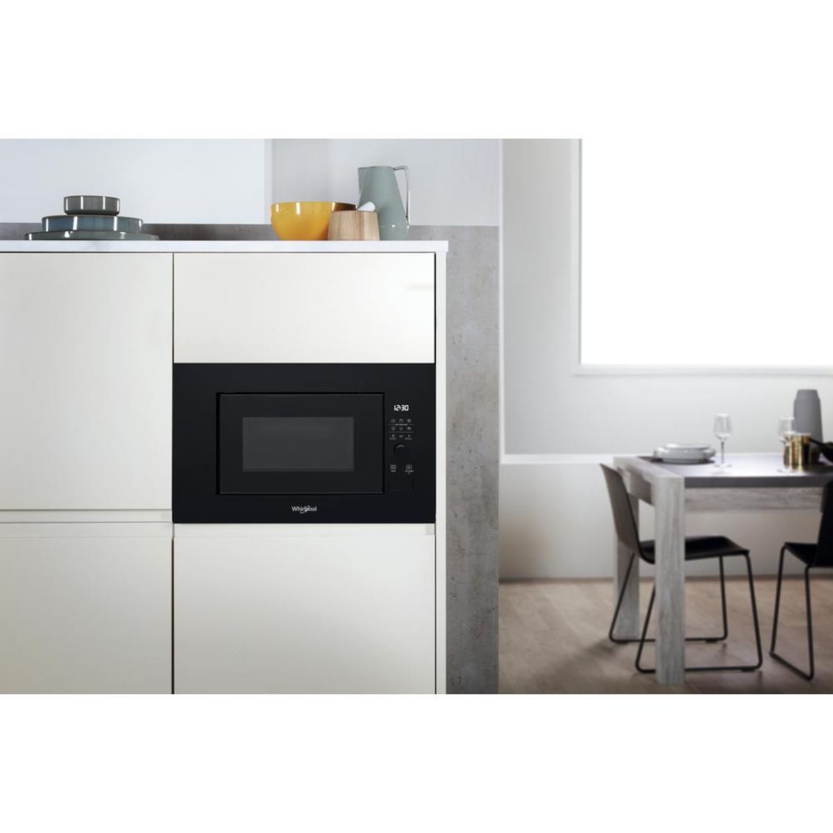 Ingebouwde zwarte magnetron in een keukenkast, met een tafel en stoelen.