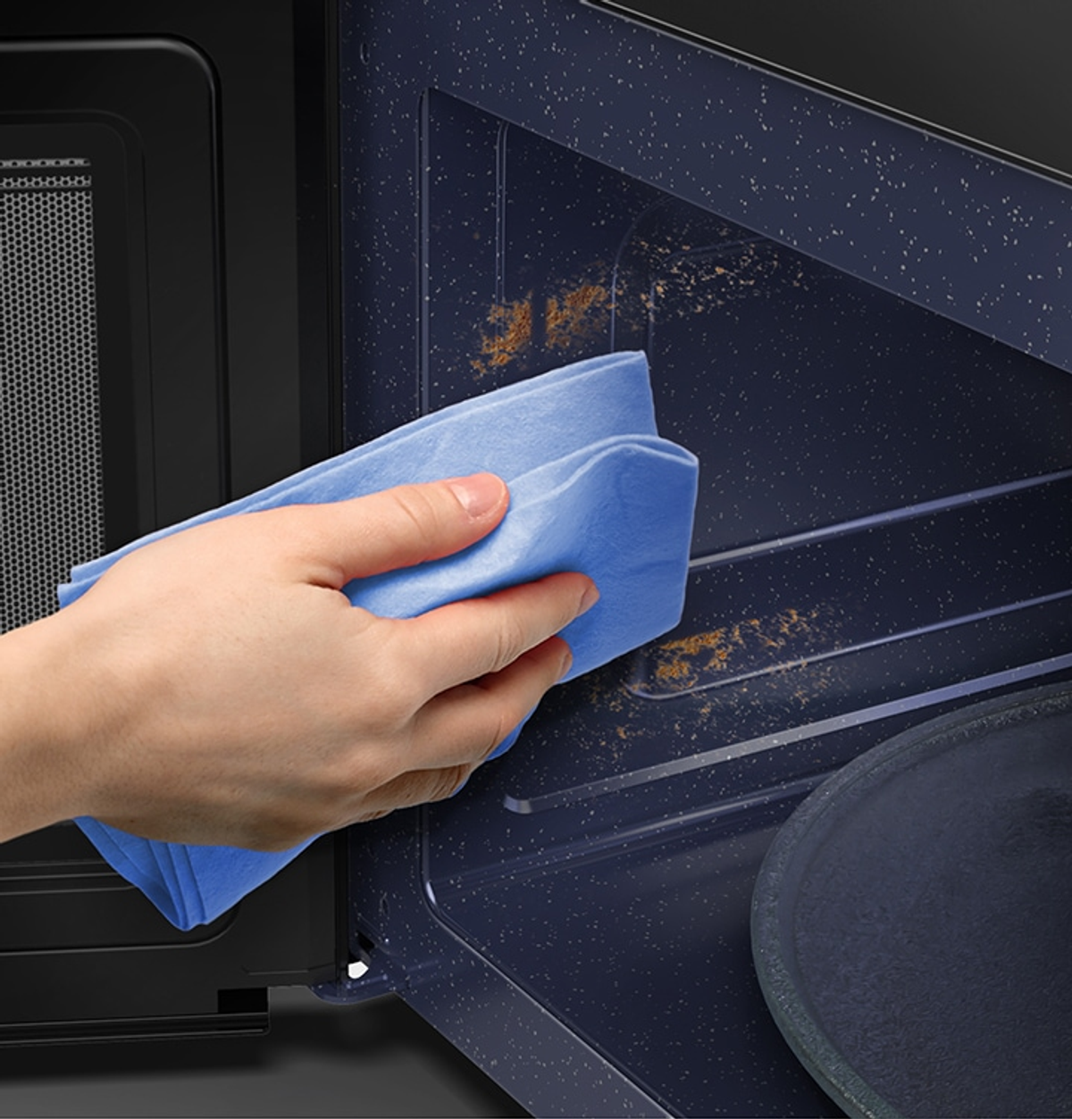 Ręka czyszcząca wnętrze kuchenki mikrofalowej. Używana jest niebieska szmatka.