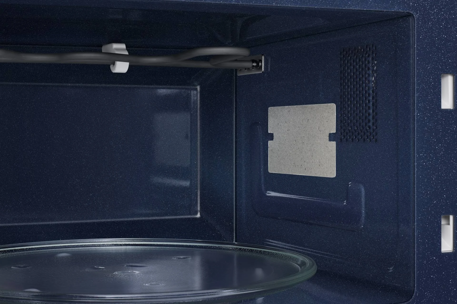 Wewnątrz ciemnoniebieskiej kuchenki mikrofalowej widoczny jest szklany talerz i element grzejny.