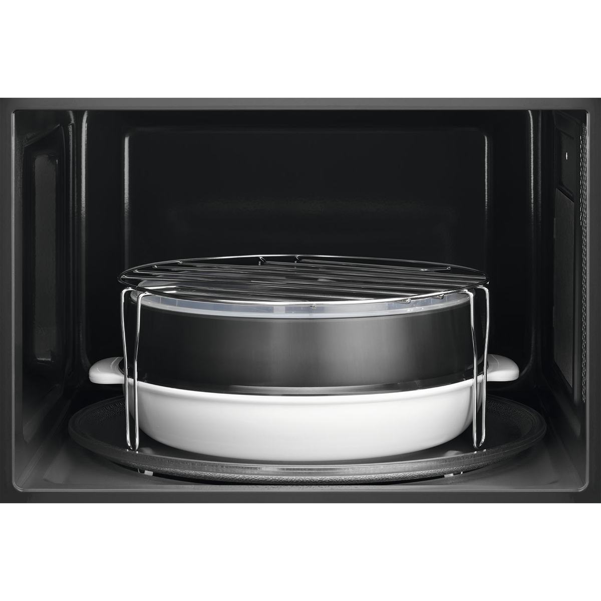 Binnenin een zwarte magnetron. Er staan ​​gestapelde gerechten op een metalen rek, klaar om te koken.