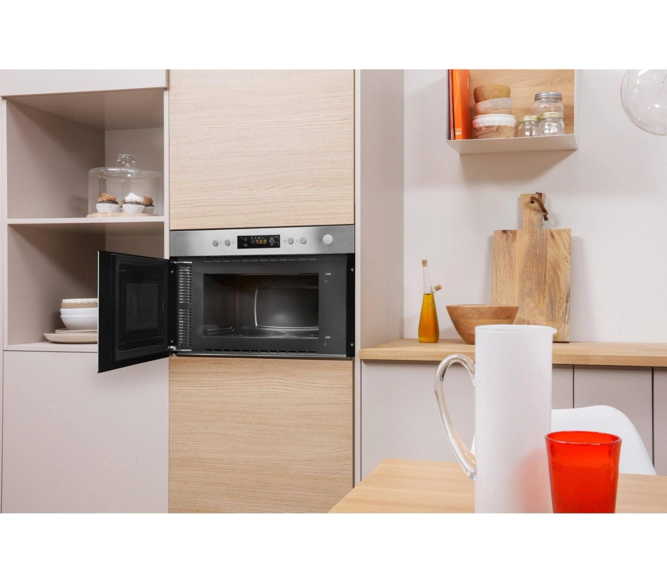 Microondas instalado en un armario de cocina con puerta abierta, utensilios de cocina y mesa de madera.