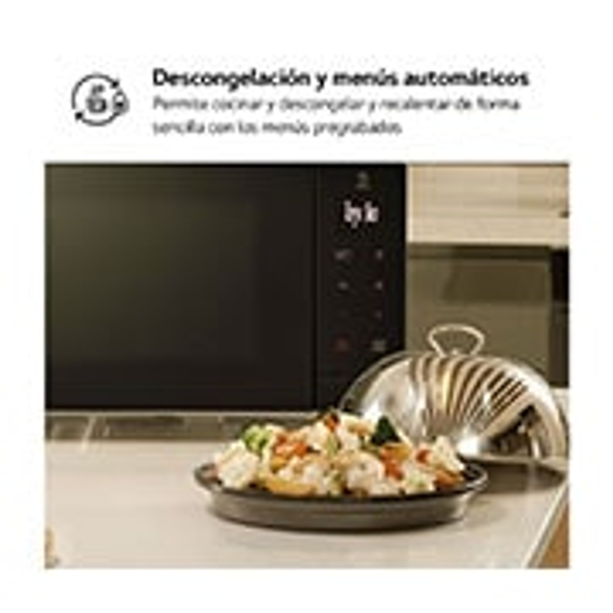 Kuchenka mikrofalowa z jedzeniem w środku, srebrna pokrywa, na białym stole.