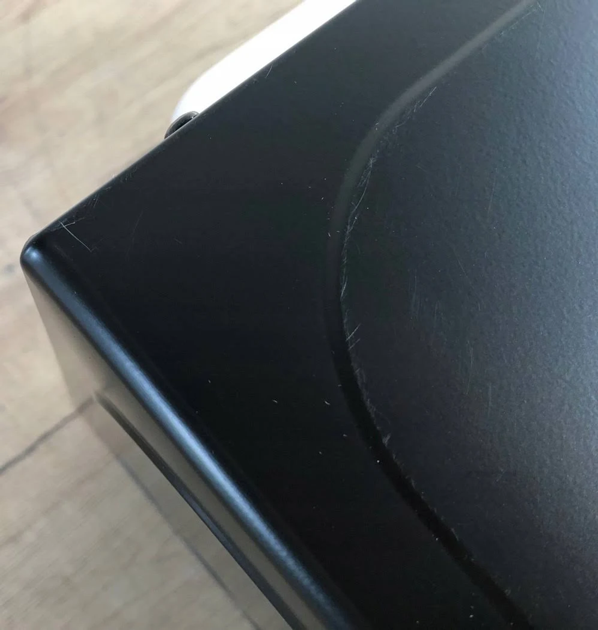 Primer plano de una esquina de microondas negro sobre madera. El negro es un color prominente. Algunos arañazos son visibles.