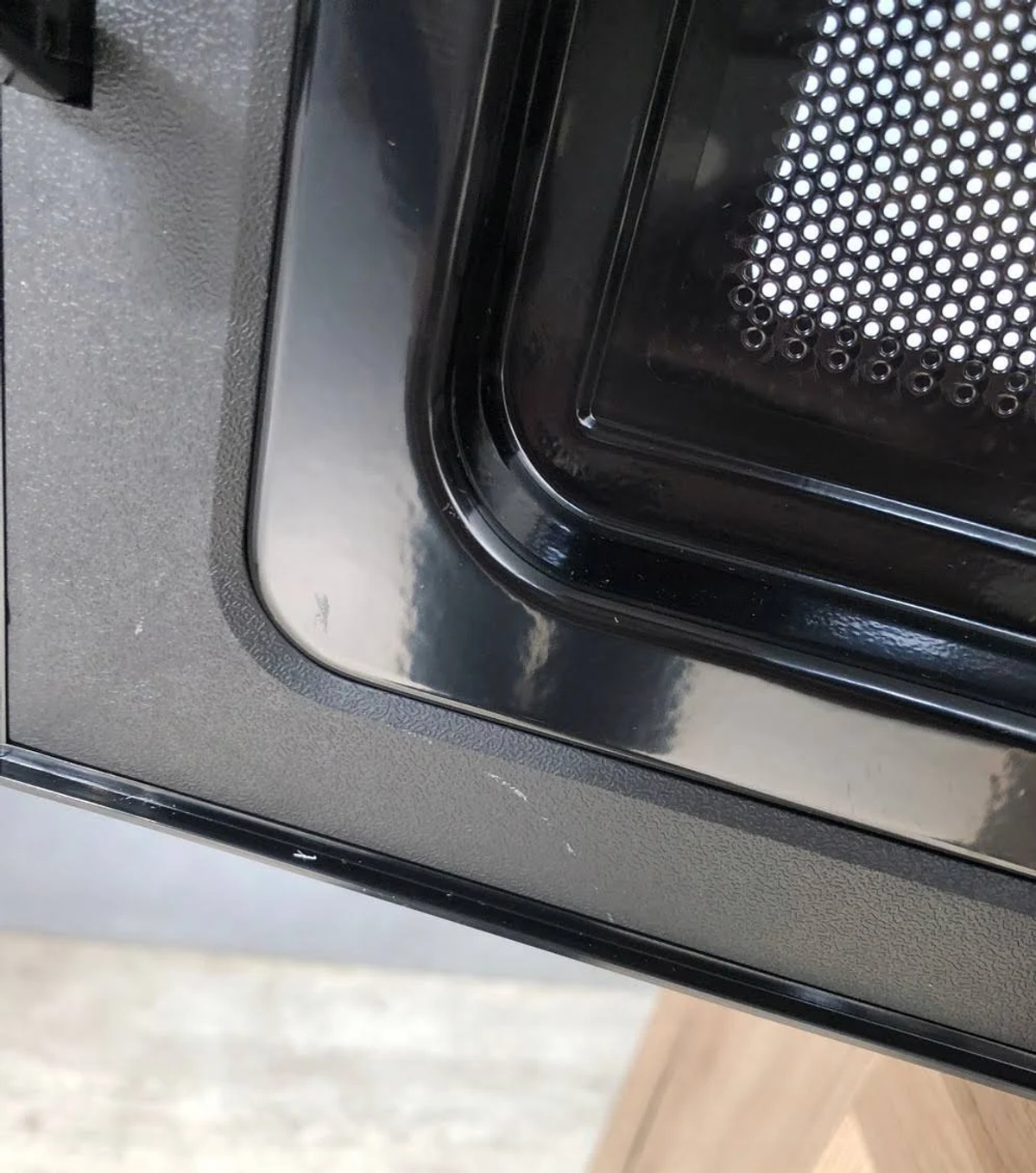 Primer plano de la puerta de un microondas, negra con superficie reflectante. La puerta está parcialmente abierta.