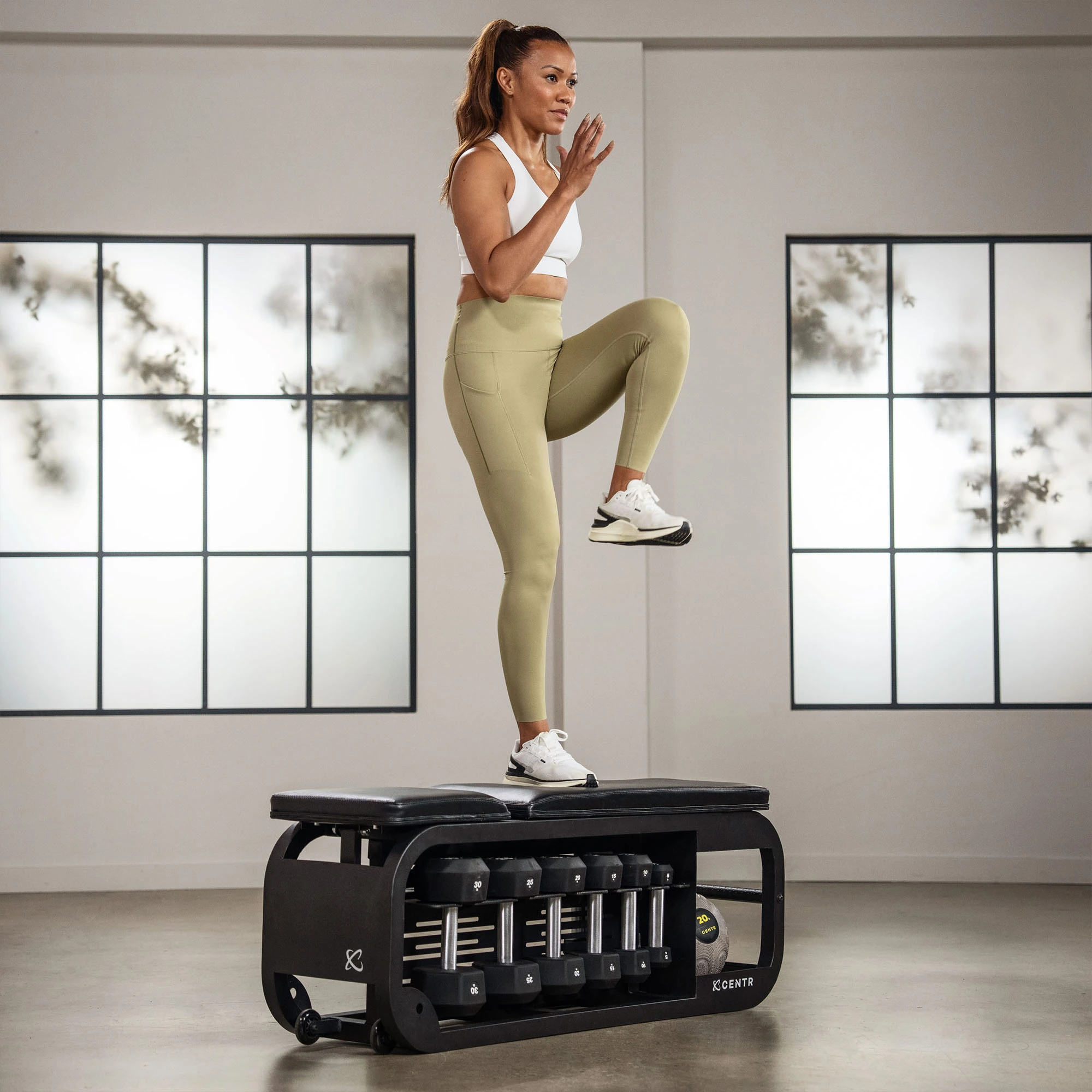 Woman exercising on a bench with weights. She is wearing workout clothes and lifting her legs.