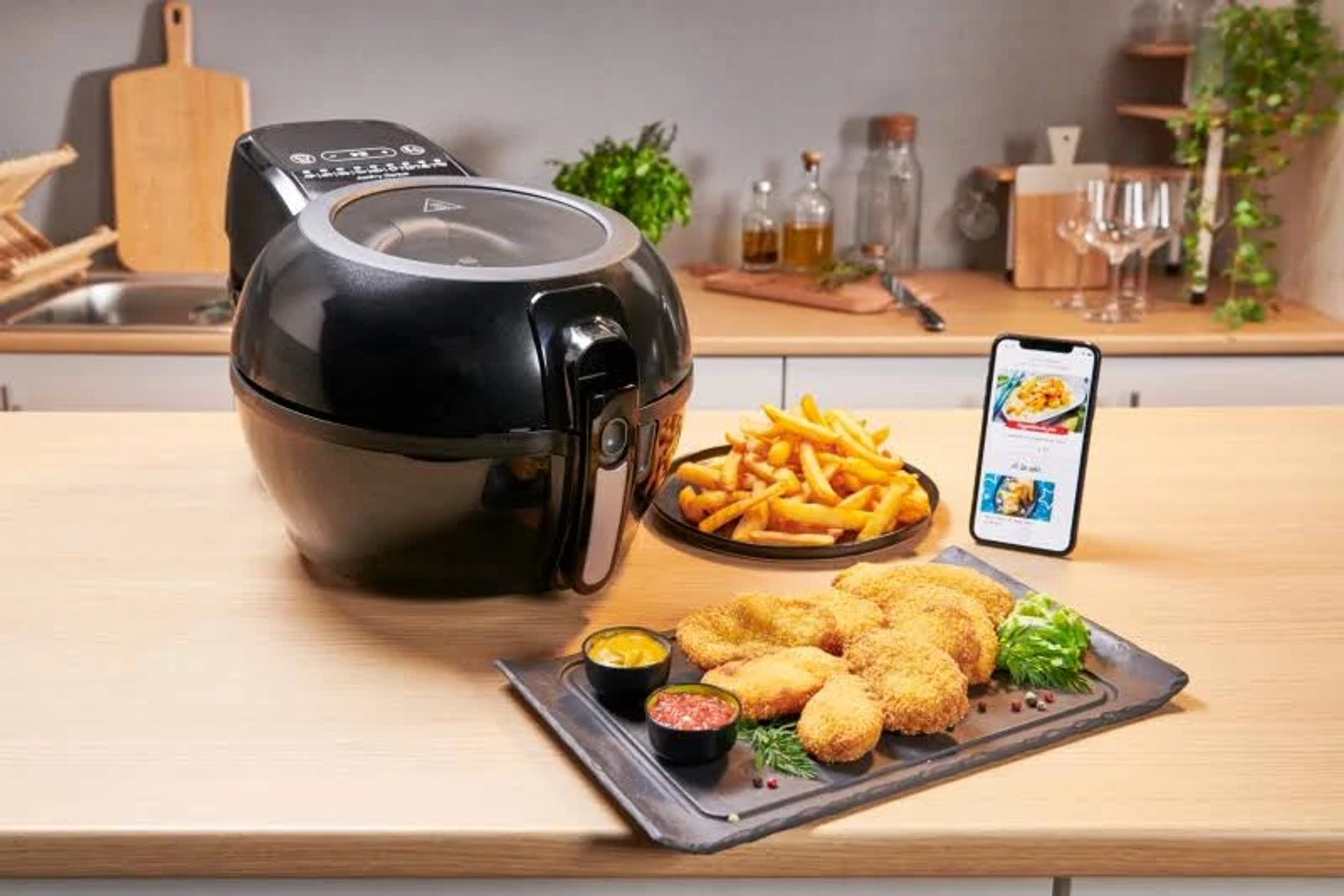 Czarna frytkownica powietrzna z frytkami, nuggetami z kurczaka i sosami na drewnianym stole. Telefon ze zdjęciem jedzenia.