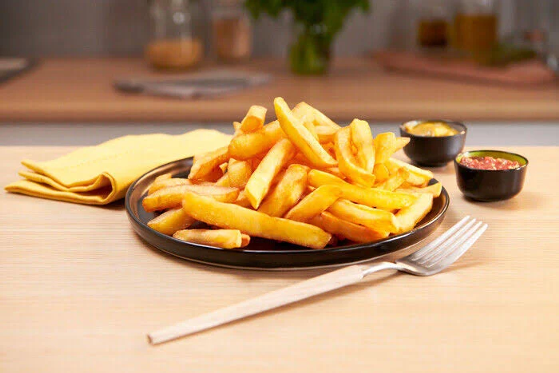 Talerz frytek z sosami do maczania. Widelec na drewnianym stole, czarny talerz.