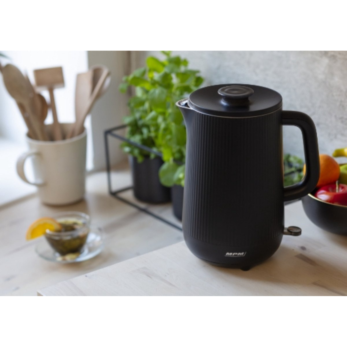 Schwarzer Wasserkocher mit einer Tasse Tee mit Zitrone und Pflanzen.
