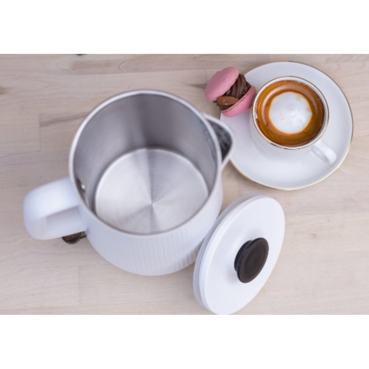Un bollitore elettrico bianco con manico e coperchio, e una tazza di caffè e un macaron.