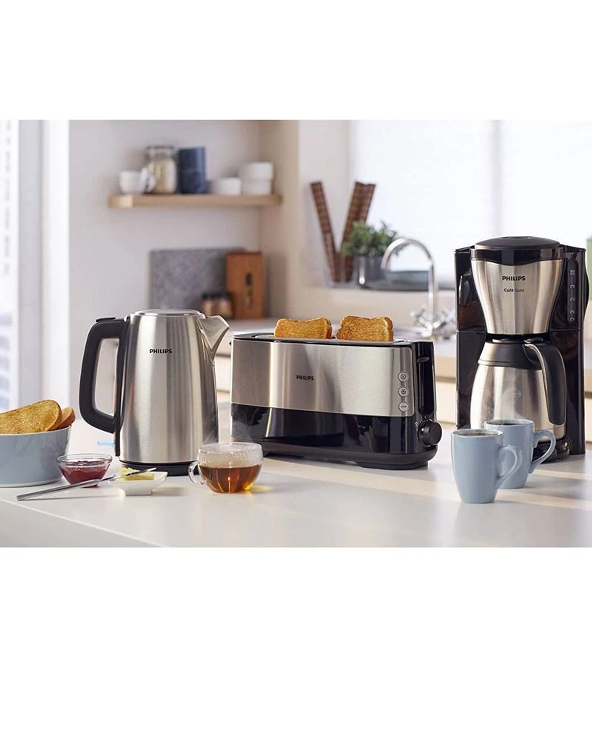 Elettrodomestici da cucina: bollitore, tostapane con toast, macchina caffè. Tazze sul bancone. Brillante.