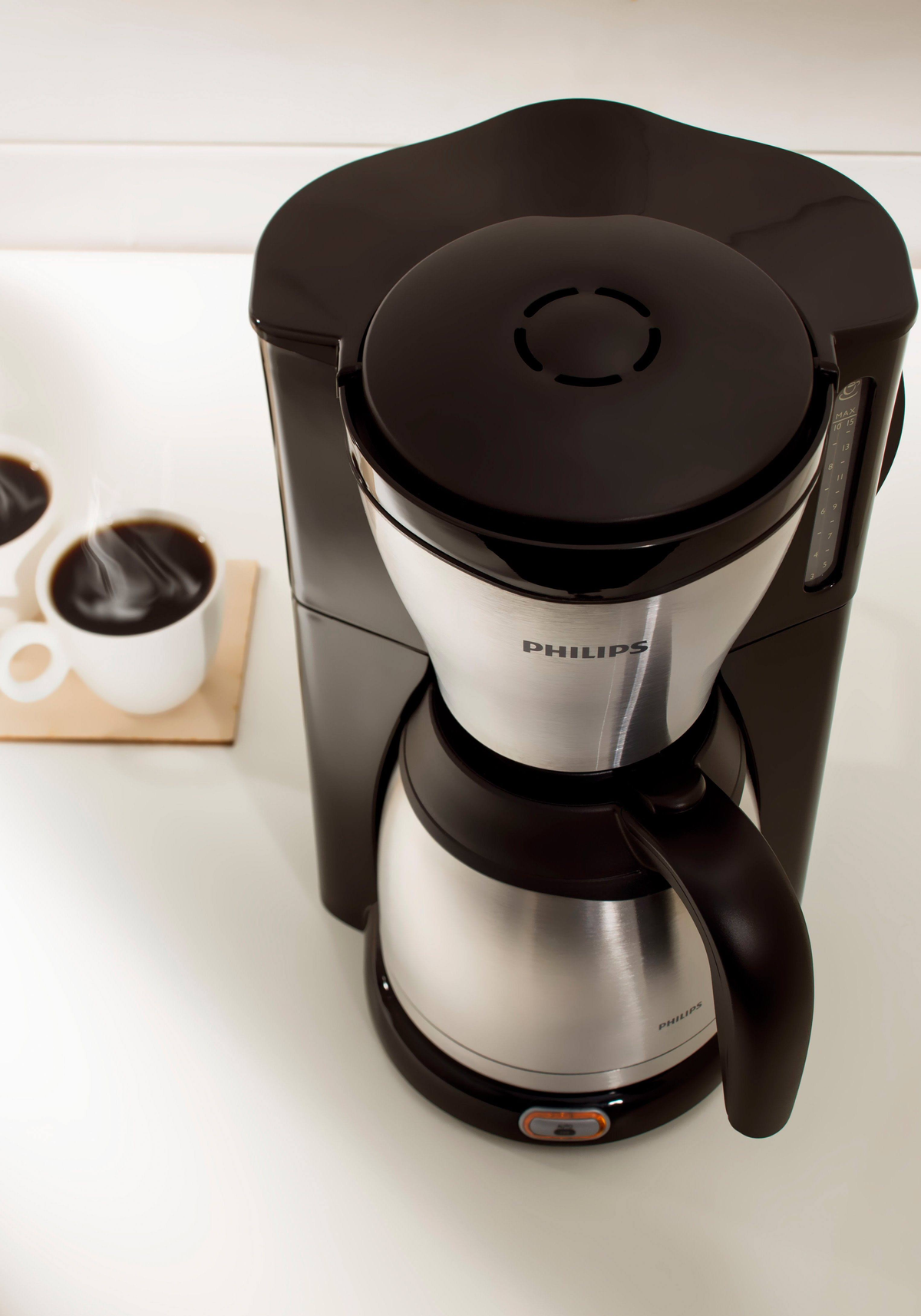 Caffettiera con tazze di caffè su superficie bianca, con caffettiera, marchio Philips, vista dall'alto.