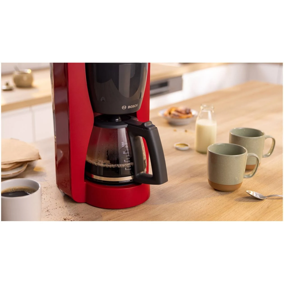 Czerwony ekspres do kawy ze szklaną karafką wypełnioną kawą, obok filiżanek i mleka.