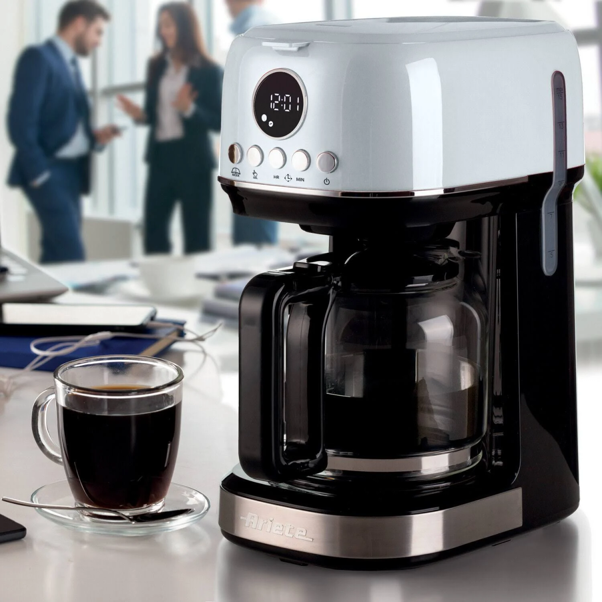 Ekspres do kawy z przezroczystą karafką i filiżanką kawy na stole.