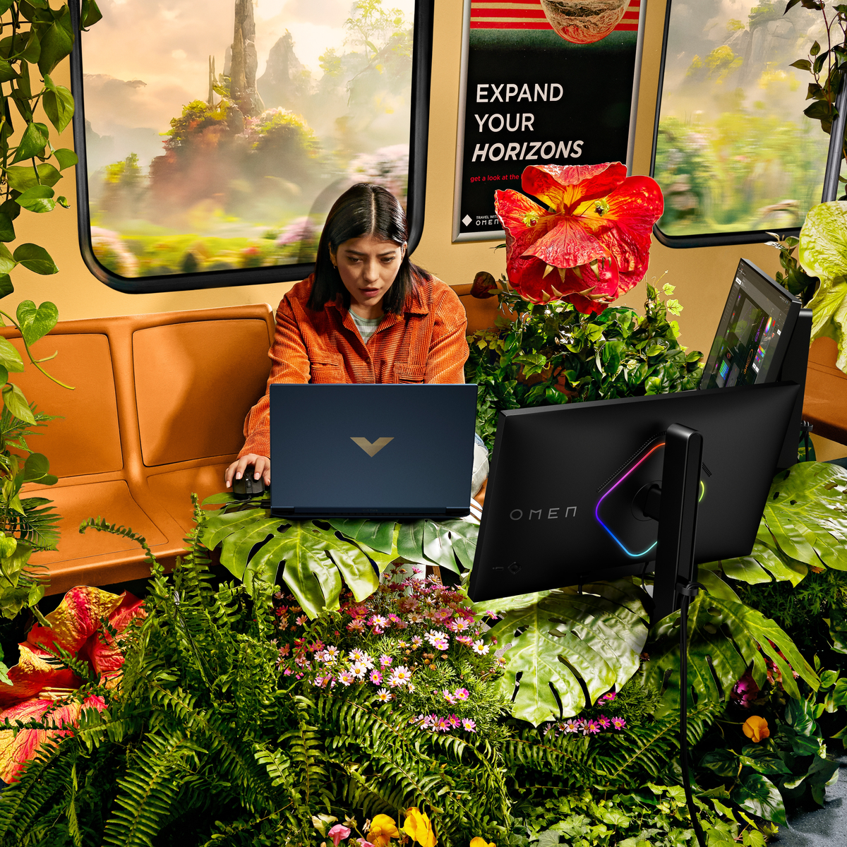 Kobieta używająca laptopa w wagonie kolejowym otoczona roślinami i dużym monitorem.