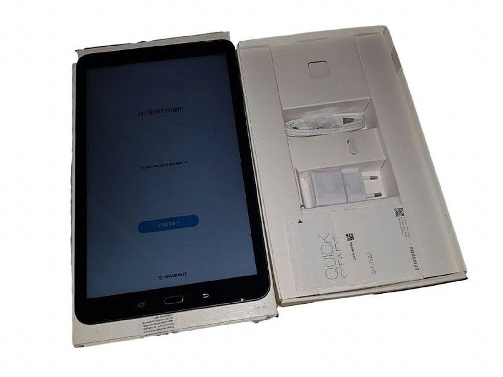 Tablet in weißer Box, offen. Der Bildschirm ist an. Text lautet 'Willkommen!' und 'Starten <gt/>'.