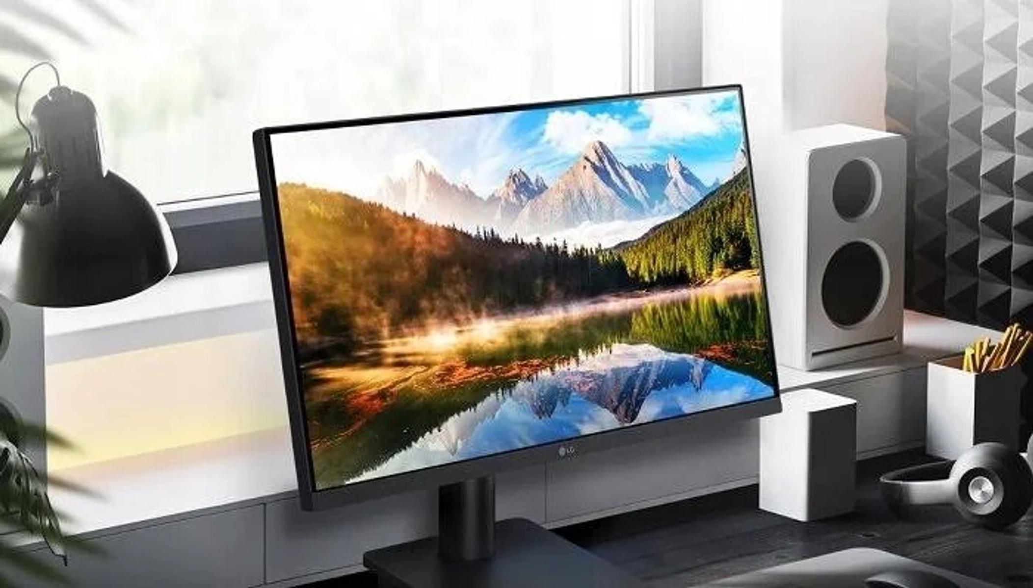 Monitor che mostra un paesaggio montano. Lampada e altoparlante sulla scrivania.