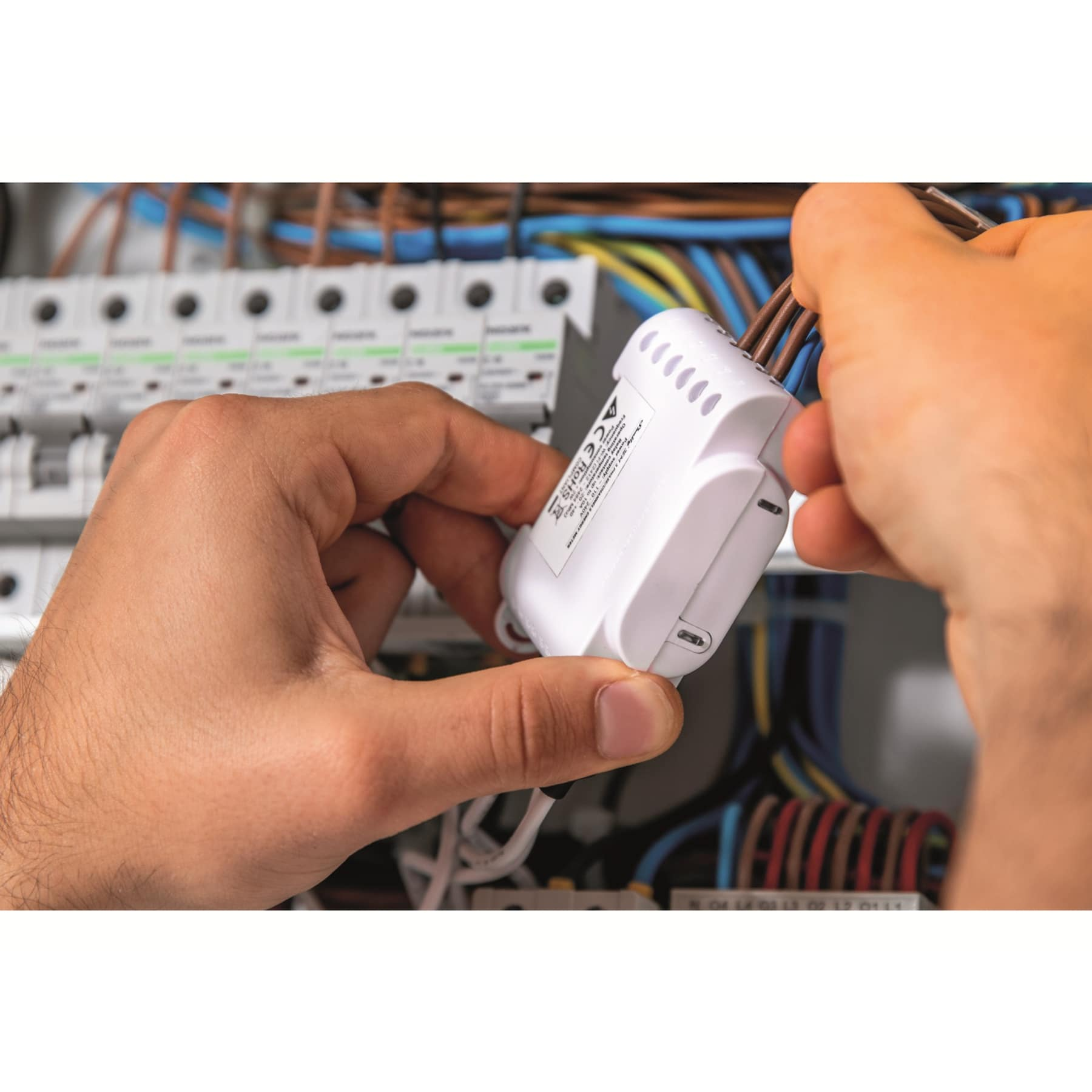 Una persona conecta cables a un pequeño dispositivo electrónico blanco, manos en primer plano.