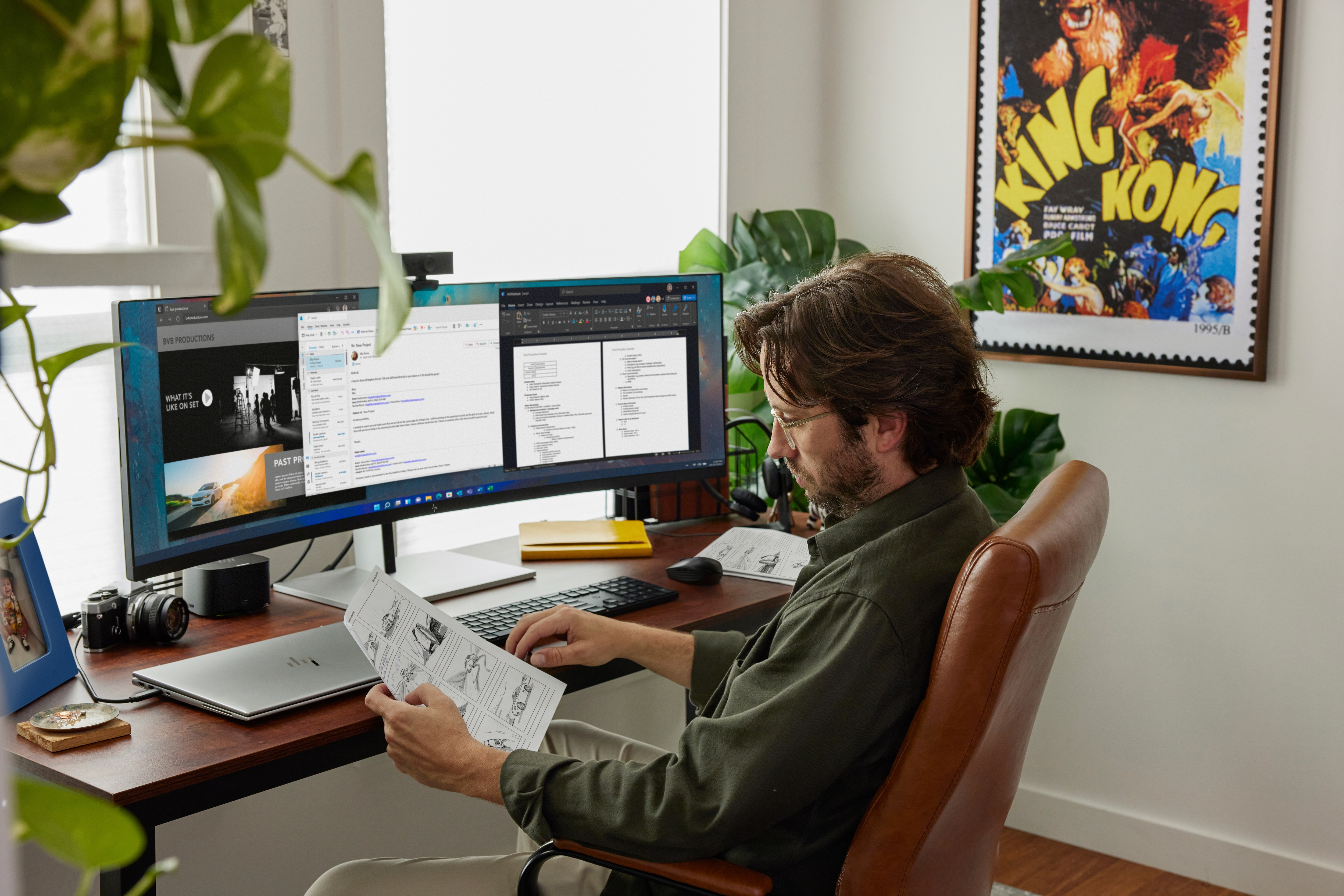 Mężczyzna siedzi przy biurku z dwoma monitorami, czytając dokument i pracując.