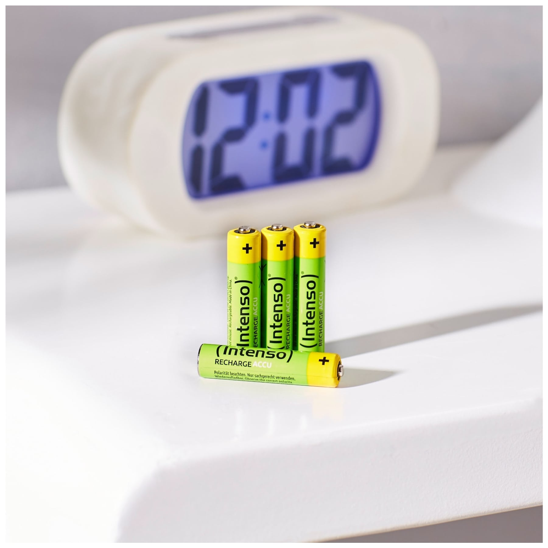 Tre batterie verdi e gialle accanto a un orologio digitale su una superficie bianca.