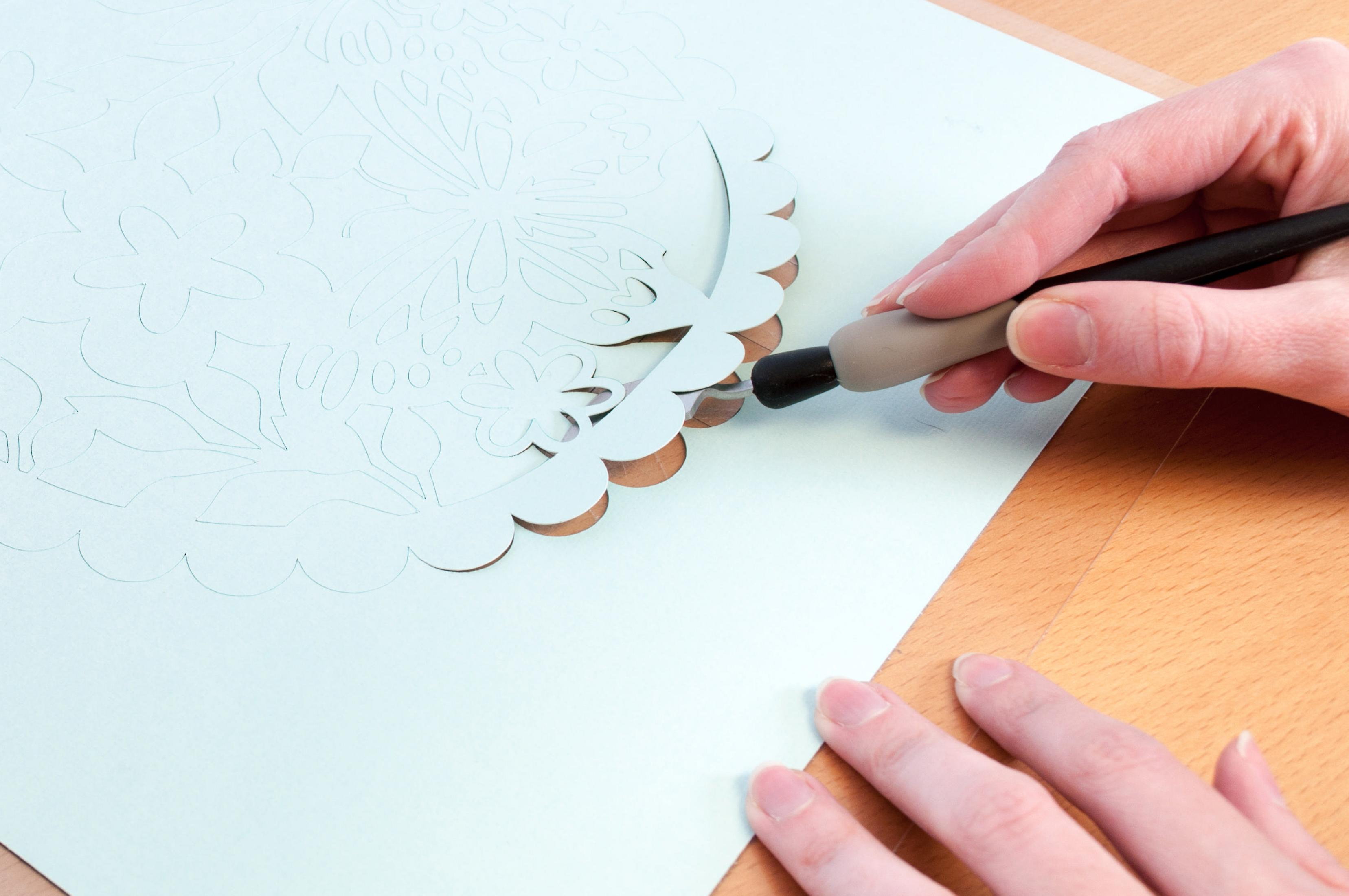 Hände schneiden Papier mit floralen Ausschnitten auf Holzoberfläche.