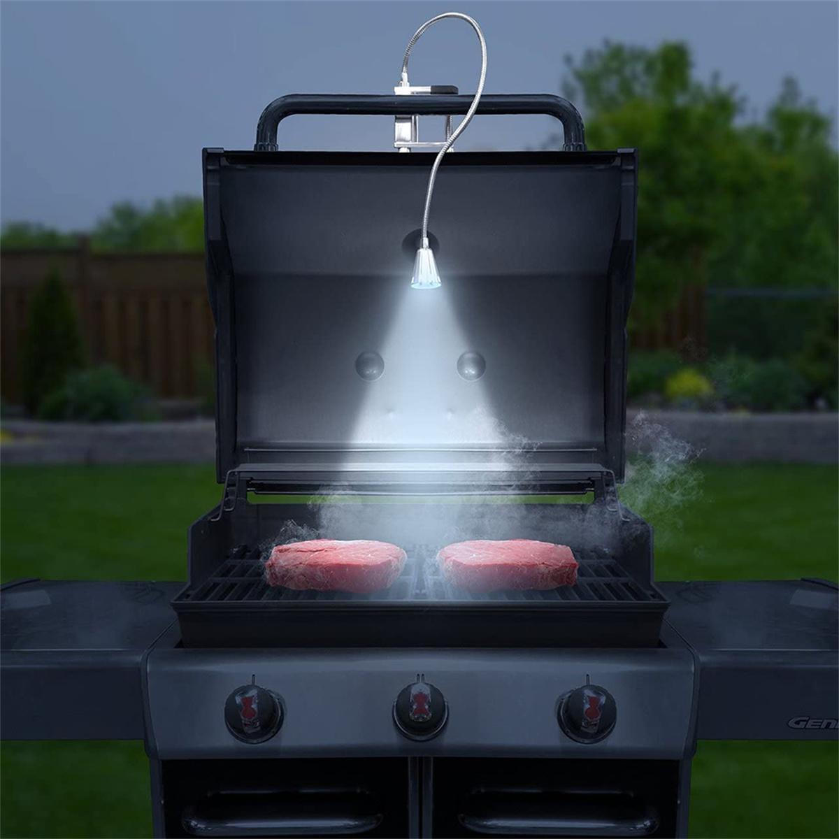 Grill mit brutzelnden Steaks. Ein Licht scheint von oben herab.