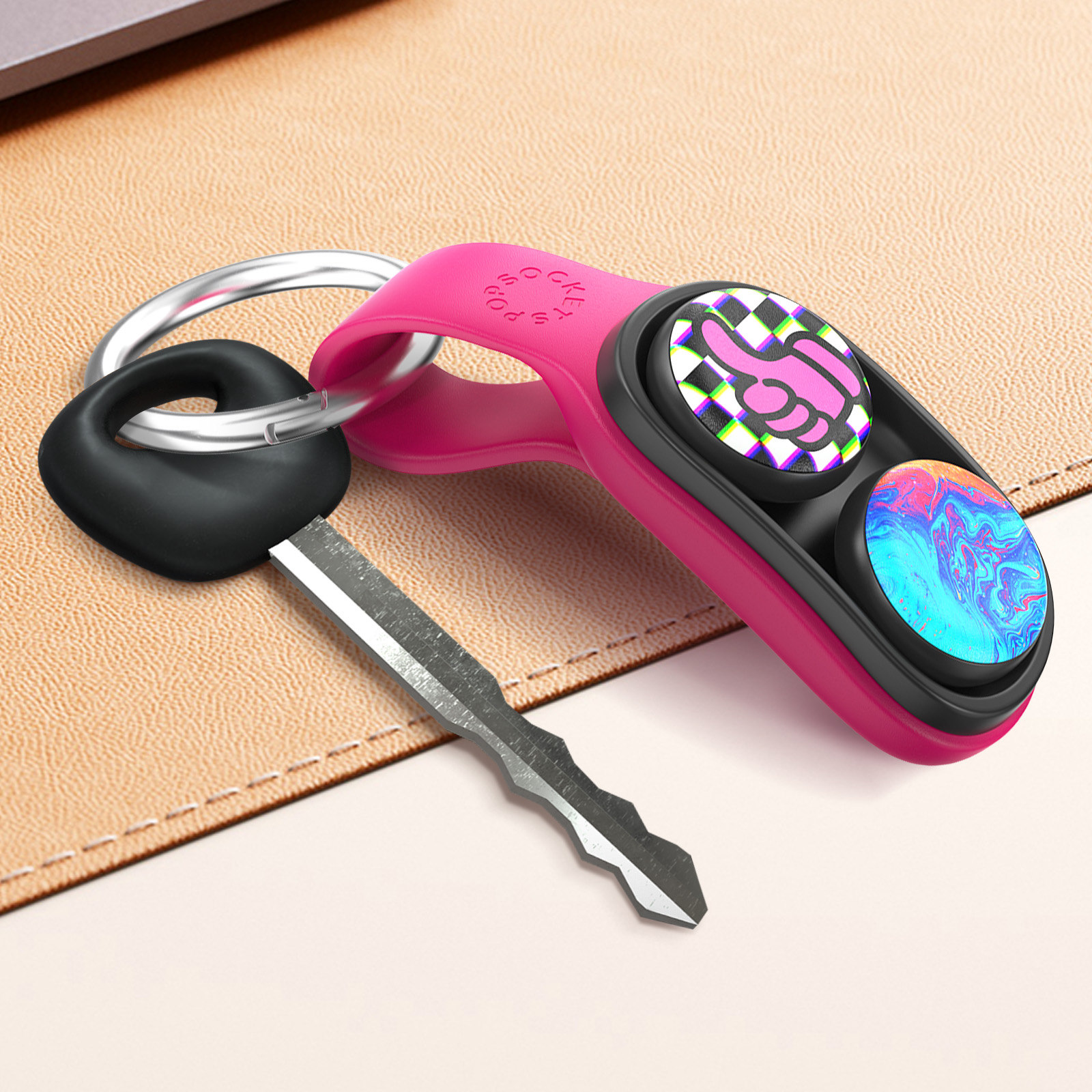 Portachiavi rosa con chiave ed etichetta PopSockets con pollice su e motivi a vortice su superficie beige.