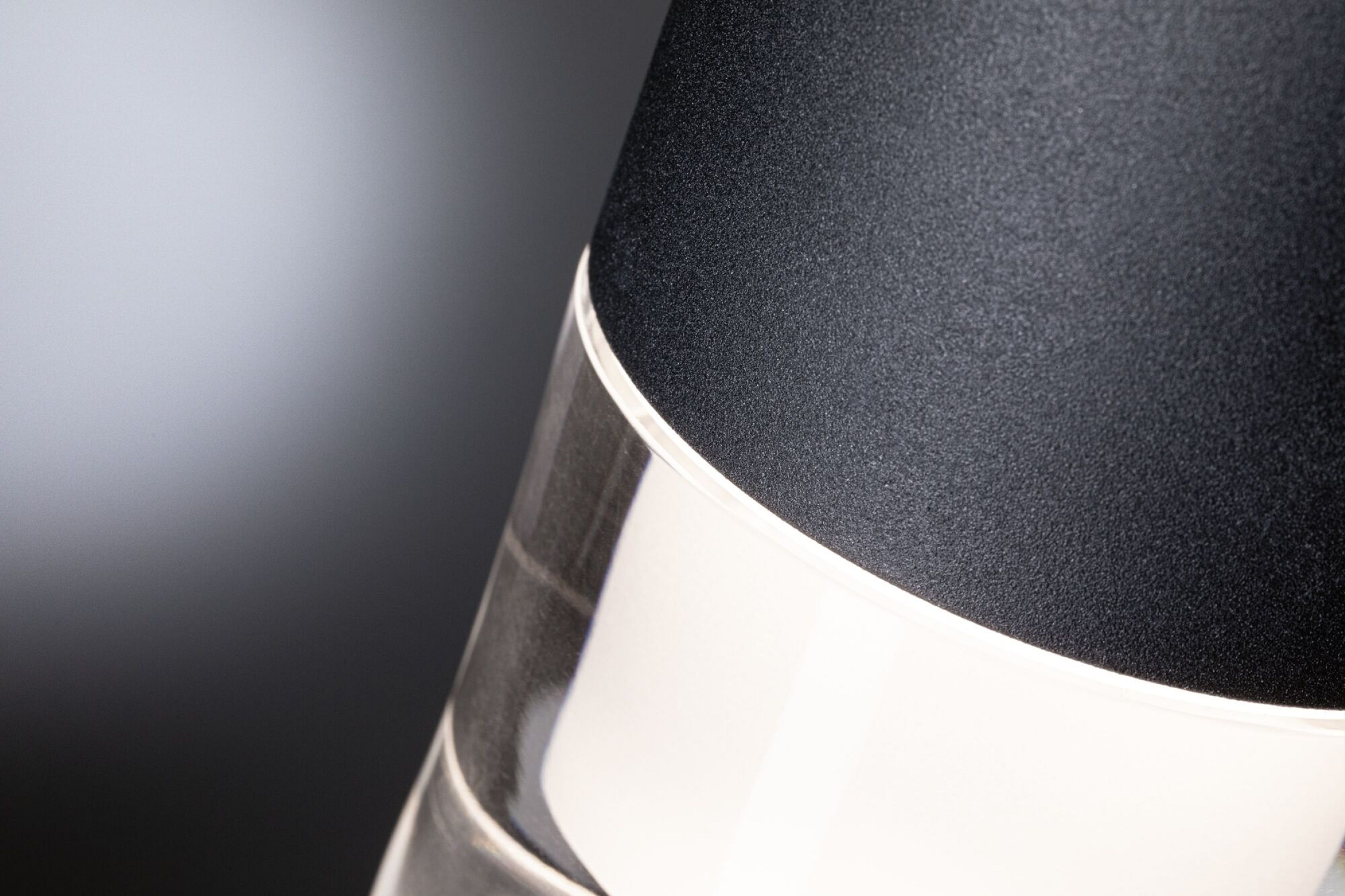 Przezroczysta szklana butelka i czarna zakrętka na tle ciemnoszarego gradientu.