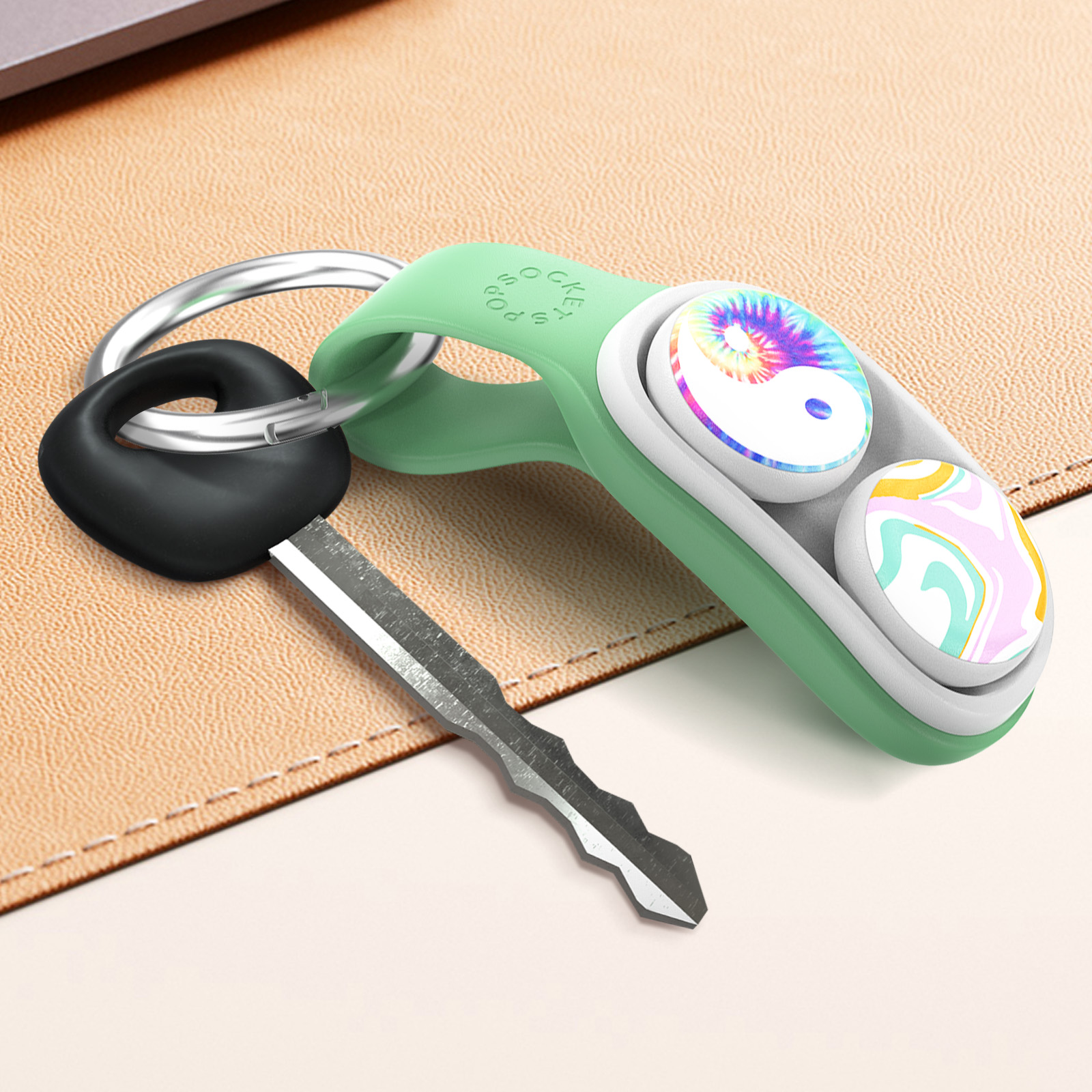 Portachiavi verde con inserti Yin-Yang e motivo a spirale, chiave nera e superficie beige.