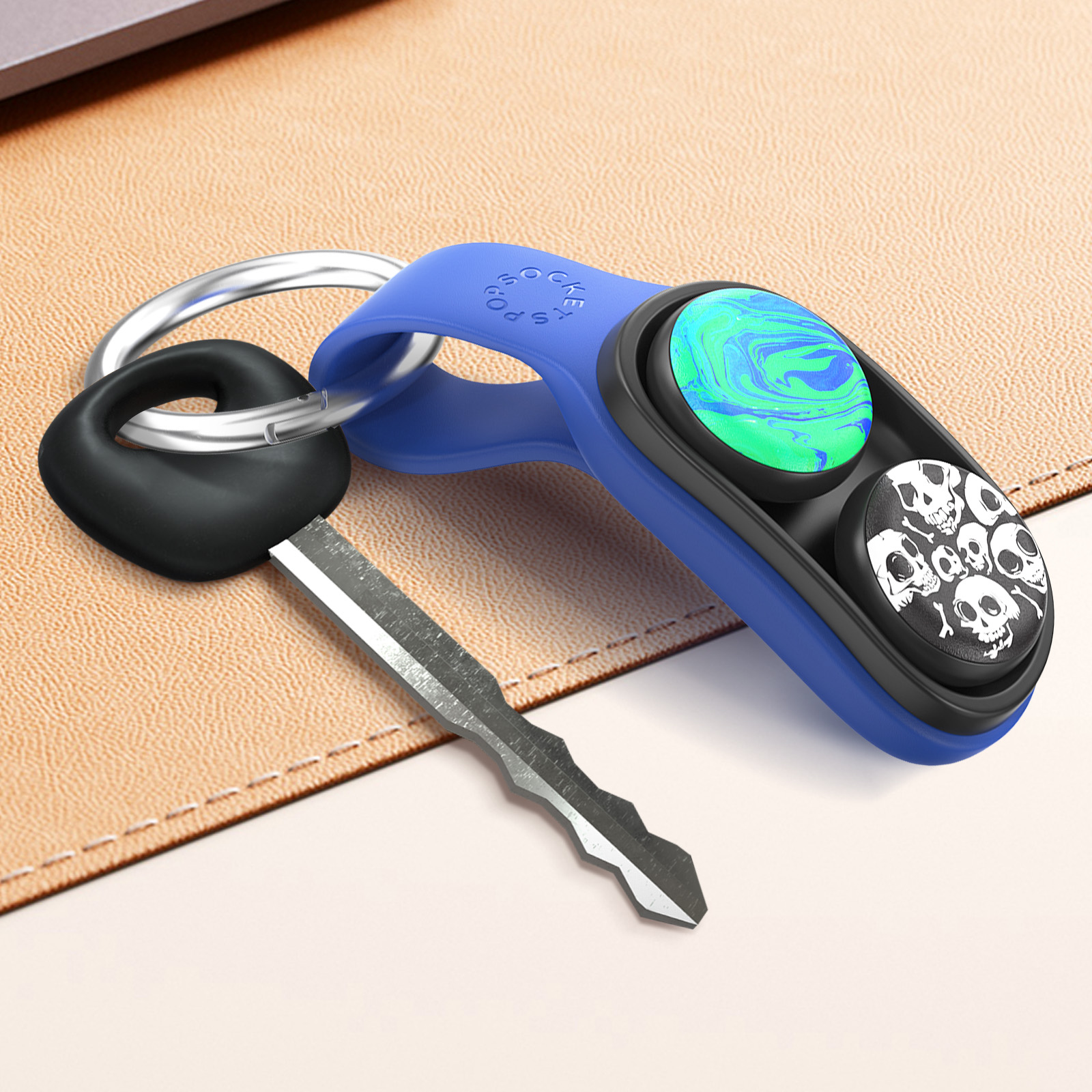 Portachiavi blu con inserti a spirale e teschio, chiave nera su superficie beige. Un laptop sullo sfondo.