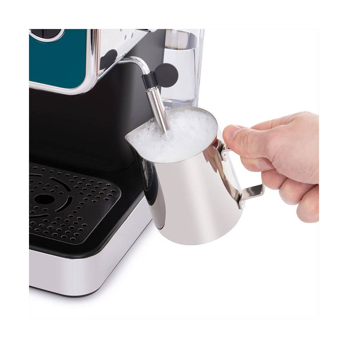 Eine Hand schäumt Milch in einen Edelstahlkrug von einer Kaffeemaschine.