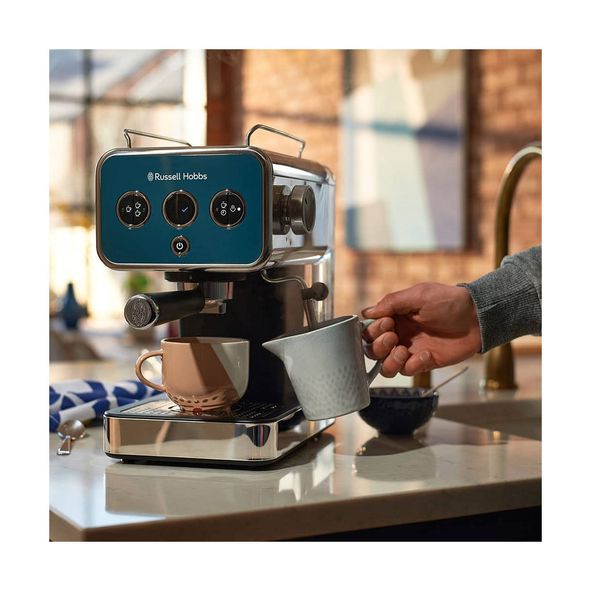 Eine Espressomaschine mit blauem Bedienfeld, eine Hand gießt Milch in eine Tasse.