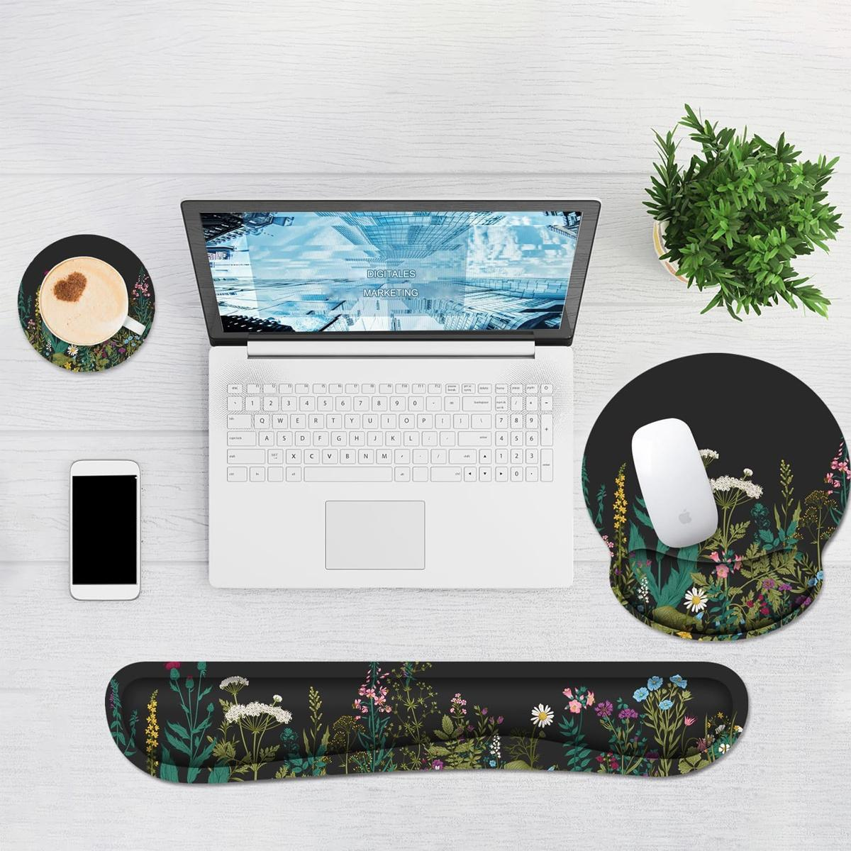 Laptop auf weißem Schreibtisch mit Zubehör: Maus, Mauspad, Untersetzer, Telefon und einer kleinen Pflanze.